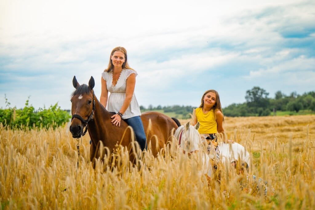 Praticienne bien-être animal avec deux chevaux dans un champ de blé