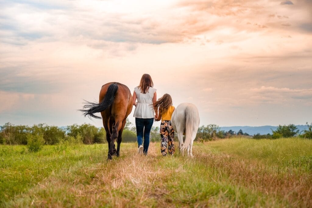 Praticienne bien-être animal avec une jeune fille marchant dans l'herbe avec deux chevaux