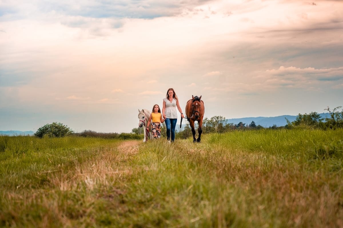 Praticienne bien-être animal avec une jeune fille, marchant dans la nature avec les chevaux